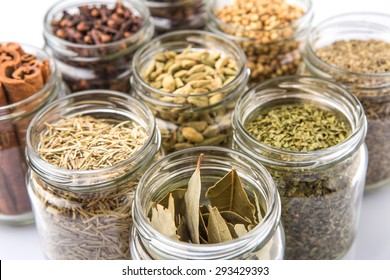 Cardamom, star anise, cinnamon, clove, coriander seed spices and dried bay leaves, parsley, thyme, rosemary herbs in mason jars over white background - Powered by Shutterstock