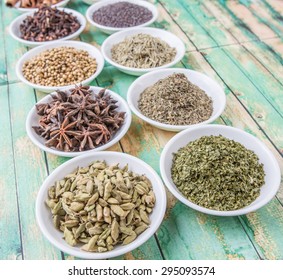 Cardamom, star anise, cinnamon, clove, coriander seed spices and parsley, thyme, rosemary herbs in white bowls over weathered wooden background - Shutterstock ID 295093574