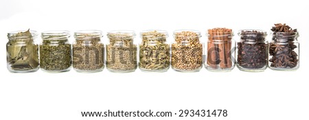 Cardamom, star anise, cinnamon, clove, coriander seed spices and dried bay leaves, parsley, thyme, rosemary herbs in mason jars over white background