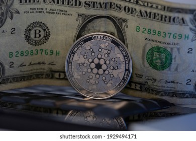 Cardano ADA Cryptocurrency Physical Coin Placed On Computer Keyboard With One Dollar Bill In The Background