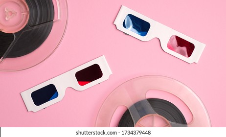 Cardboard 3d glasses and reels of film on pink background. Watching movie at cinema concept.