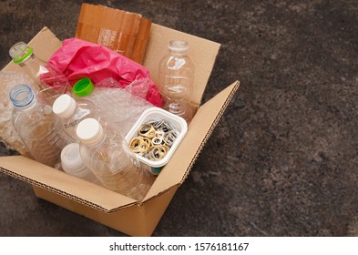 Cardboard Box Or Carton Filled With Plastic Bottle , Plastic Bag ,waste Paper ,ring Pull Or Pull Tab , On Dark Concrete Background  Wait For Reuse Or Recycle , Save Environment And Green Concept 