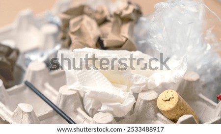 A cardboard box is filled with trash, including a napkin, a plastic bag, and a cork