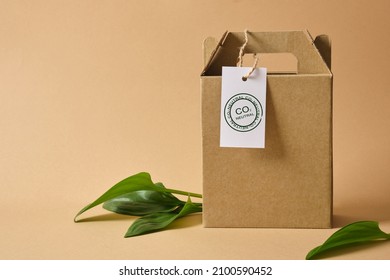 cardboard box with handles for delivery or gift, leaves and white tag marked co2 neutralon brown background Eco friendly packaging, paper recycling, zero waste, natural products concept. Copy space. - Shutterstock ID 2100590452
