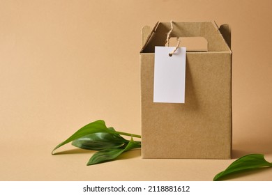 cardboard box with handles for delivery or gift, leaves and white mockup blank tag for marking or inscription Eco friendly packaging, paper recycling, zero waste, natural products concept. - Shutterstock ID 2118881612