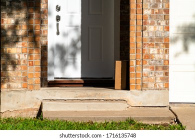 Cardboard Box Left On Doorstep Of A Brick Home In An Established Neighborhood. A Delivery Service Leaving Package At Front Doorstep Or Porch Of Nice Home 