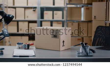 Cardboard Box Package Standing on the Table of the Warehouse where Rows of Shelves with Parcels Waiting to be Shipped and Delivered.