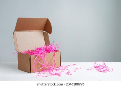 Cardboard Box With Pink Crinkle Cut Paper Shred Filler For Safe Delivery On The Table. Background With Copy Space.