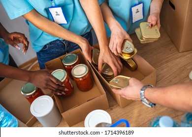 Cardboard boxes being filled with food donations. Helpful team of social workers. Young people volunteering to sort donations for charity food drive. Unrecognizable people volunteering in food bank - Powered by Shutterstock