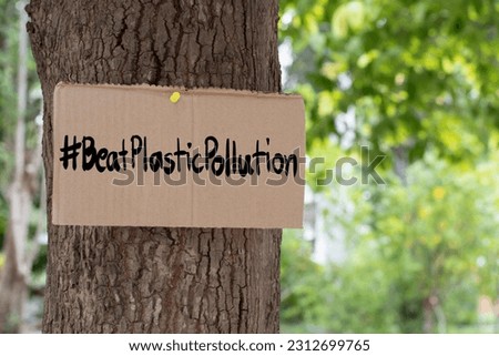 Cardboard from boxes cover with texts '#BeatPlasticPollution', 2023 world environment day motto, was sticked on tree bark to call out all people to care about and to beat the pollution from plastic.
