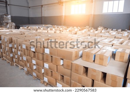 A lot of cardboard boxes with finished products with sweets stand in a warehouse against the backdrop of a window with a sunset. Industry