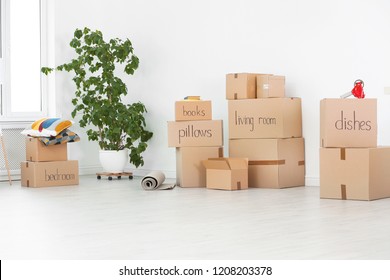 Cardboard boxes and household stuff near white wall indoors. Moving day - Shutterstock ID 1208203378
