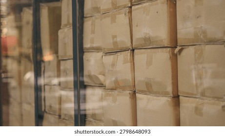 Cardboard boxes stacked inside distribution warehouse behind glass window close up.