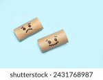 Cardboard center of a toilet paper rolls without paper with and sad faces drawn on a blue background with copy space