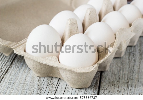 Cardboard egg\
rack with eggs on white wooden\
table