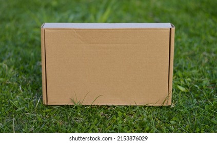 Cardboard Large Parcel Box On The Background Of Green Grass Outdoors. Mock Up Of Packaging Of Environmentally Friendly Products