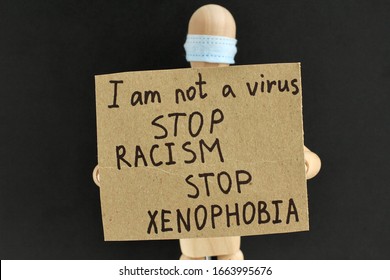 Cardboard Sign With Text In The Hands Of A Wooden Doll Or Mannequin In A Medical Mask. Concept Of Anti Racism, Anti Xenophobia, The Social Situation Around The Coronavirus Or Covid-19.