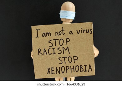 Cardboard Sign With Text In The Hands Of A Wooden Doll Or Mannequin In A Medical Mask. Concept Of Anti Racism, Anti Xenophobia, The Social Situation Around The Coronavirus Or Covid-19.