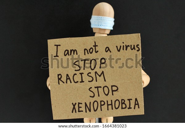 Cardboard\
sign with text in the hands of a wooden doll or mannequin in a\
medical mask. Concept of anti racism, anti xenophobia, the social\
situation around the Coronavirus or\
Covid-19.