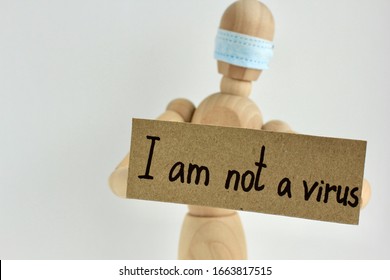 Cardboard Sign With Text I Am Not A Virus In The Hands Of A Wooden Doll Or Mannequin In A Medical Mask. Concept Of Anti Racism, Anti Xenophobia, The Social Situation Around The Coronavirus Or Covid-19