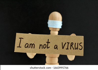 Cardboard Sign With Text I Am Not A Virus In The Hands Of A Wooden Doll Or Mannequin In A Medical Mask. Concept Of Anti Racism, Anti Xenophobia, The Social Situation Around The Coronavirus Or Covid-19