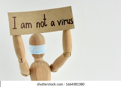 Cardboard Sign With Text I Am Not A Virus In The Hands Of A Wooden Doll Or Mannequin In A Medical Mask. Concept Of Anti Racism, Anti Xenophobia, The Social Situation Around The Coronavirus Or Covid-19