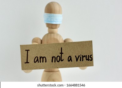 Cardboard Sign With Text I Am Not A Virus In The Hands Of A Wooden Doll Or Mannequin In A Medical Mask. Concept Of Anti Racism, Anti Xenophobia, The Social Situation Around The Coronavirus Or Covid-19