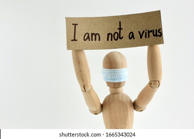 Cardboard Sign With Text I Am Not A Virus In The Hands Of A Wooden Doll Or Mannequin In A Medical Mask. Concept Of Anti Racism, Anti Xenophobia, The Social Situation Around The Coronavirus Or Covid-19