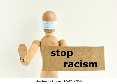 Cardboard Sign With Text Stop Racism In The Hands Of A Wooden Doll Or Mannequin In A Medical Mask. Concept Of Anti Racism, Anti Xenophobia, The Social Situation Around The Coronavirus Or Covid-19