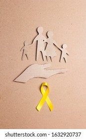 Cardboard silhouette of a family with yellow awareness ribbon on cardboard background. Suicide prevention and Childhood Cancer Awareness concept.