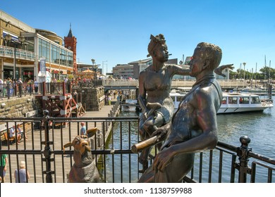 CARDIFF BAY, CARDIFF, WALES  - JULY 2018: The “People like us” bronze statue of s young couple and their dog on the waterfront of Mermaid Quay in Cardiff Bay