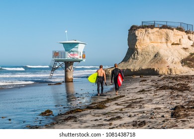 CARDIFF, CALIFORNIA/USA - APRIL 14, 2018:  Two male surfers carry surfboards near a lifeguard tower on San Elijo State Beach in Cardiff, California, located in San Diego County.