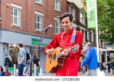 Cardiff, UK. October 2017. Young Asian Man Busking On His Guitar In The Hayes, Cardiff. He Is Wearing A Bright Red Shirt And Dungarees; And Has An Owl Earring.