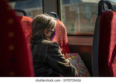 Cardiff, Wales, UK - 04.17.2021: A Train Passenger Looks Out The Window During The Journey. She Wears A Face Mask. This Is Currently Mandatory On Public Transport In UK, Due To Covid-19 (Coronavirus).