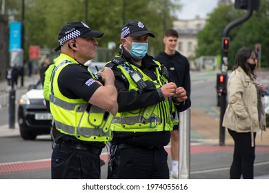 Cardiff, Wales, UK - 05.15.2021: Two Police Officers Watch A Crowd Of Protesters. One Of Them Is Wearing A Face Mask, Due To The Current Coronavirus (Covid-19) Pandemic.