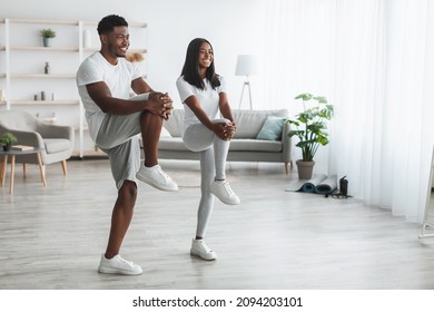 Cardio Workout. Black Couple Training Together In Living Room, Doing High Knees Exercise. Couple Warming Up Standing Lifting Leg Up To Chest, Stratching Hamstring Muscles, Looking At Free Copy Space