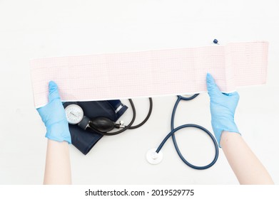 Cardiogram Of The Heart. Closeup Of The Doctor's Gloved Hands Holding ECG Paper.
