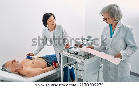 Cardiogram test. Elderly male patient receives heart rate monitored using electrocardiogram equipment with two doctors cardiologist