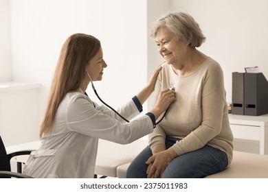 Cardiologist in coat examines older woman in clinic, listen to heartbeat with stethoscope during patient visit. Elderly woman passes heart check-up in hospital. Citizen healthcare services, cardiology - Powered by Shutterstock