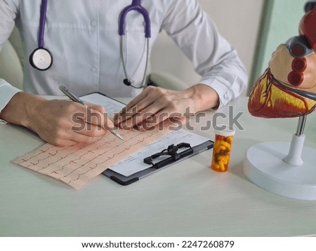 Cardiologist examines a cardiogram against background of artificial heart model. Heart failure treatment