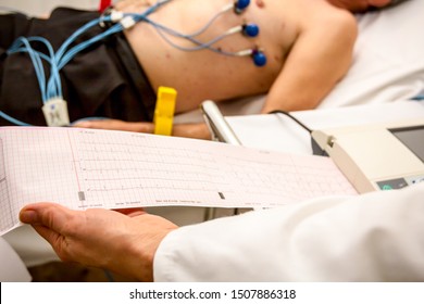 The cardiologist holding and review the electrocardiograph EKG or ECG diagram printed on grid paper.