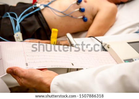 The cardiologist holding and review the electrocardiograph EKG or ECG diagram printed on grid paper.