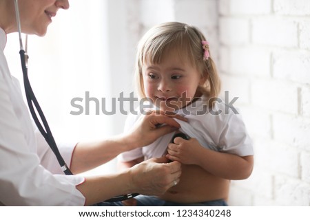 Cardiologist listens to the heart of a child with Down syndrome, the concept of health and medical examination of children with special needs