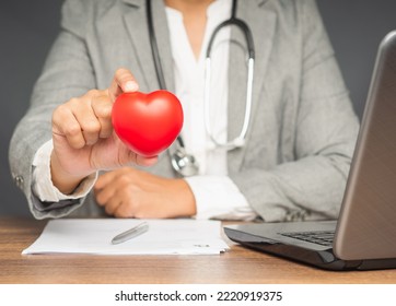 Cardiology Concept. Close-up Of Hand Doctor Holding A Red Heart Shape While Sitting At The Table In The Hospital. Close-up Photo. Health And Medical Conceptual