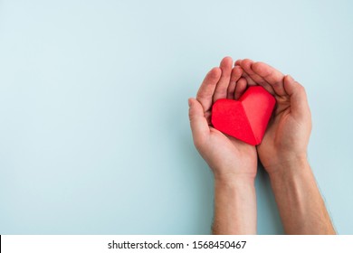Cardiology and medical concept. Man hands hold red heart on a light blue background. Top view, copy space