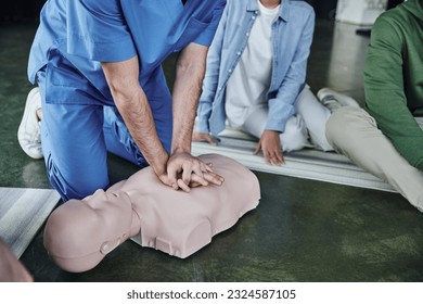 cardiopulmonary resuscitation, partial view of medical instructor doing chest compressions on CPR manikin near young participants of first aid seminar, life-saving skills and techniques concept - Powered by Shutterstock