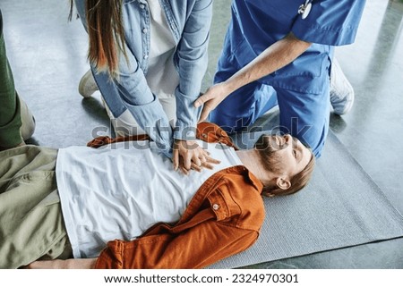 cardiopulmonary resuscitation, professional instructor helping woman practicing chest compressions on young man lying in training room, effective life-saving skills and techniques concept