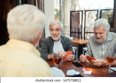 Cards With Friends. Aged Bearded Man Laughing While Playing Cards With Friends Sitting Outside Pub