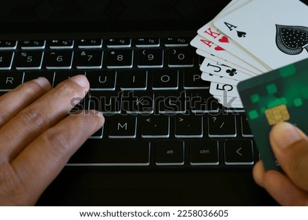 Cards kept on keyboard and hands of a person making payment for game. Online rummy, poker, casino, black jack, gambling, money, fraud, addiction, advertise, loss, profit, win, lose, cash, club, party.