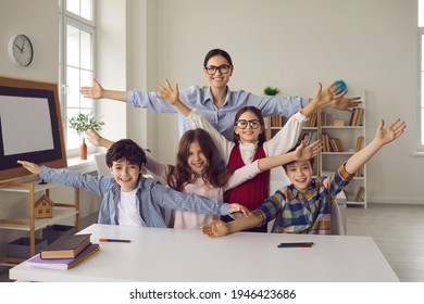 Care and adoration between educator and elementary students. Happy cheerful pupil and teacher positive portrait in classroom. Tutor and children gesturing hugs at camera showing great love emotion